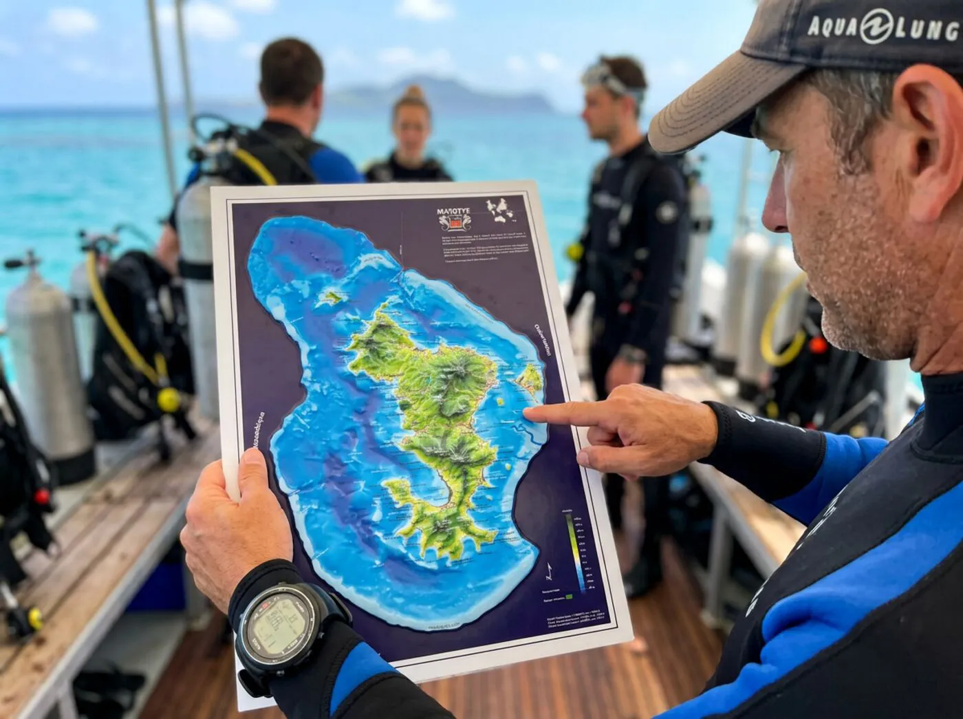 Un plongeur montre du doigt la carte de Mayotte sur le pont d'un bateau